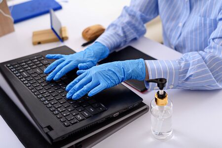close-up of hands in blue medical gloves typing on laptop, remote work at home, freelancer in quarantine conceptの写真素材