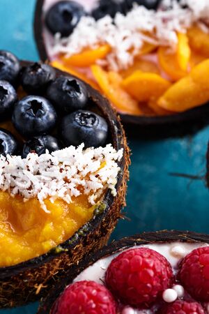 vertical smoothie bowls with berries and fruit, exotic dessert sherbet in coconut bowl on blue backgroundの写真素材