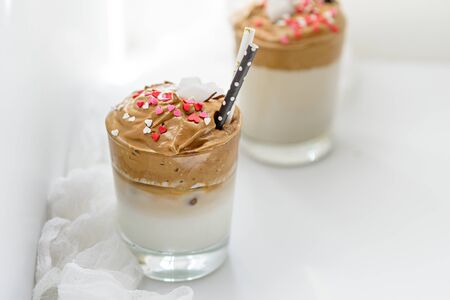 trendy Korean coffee in glasses with tubes, decorated with coconut flakes and hearts on white background, dalgona coffee conceptの写真素材