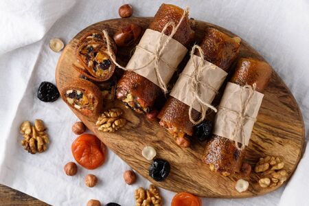 fruit pastille with dried fruits, nuts and honey wrapped in parchment paper on wooden Board on white background, healthy dessert, vegetarian snack concept, top viewの写真素材