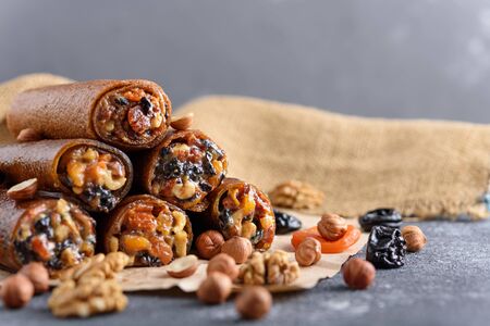 fruit roll-up with nuts, prunes, dried apricots and honey, vegetarian snack, healthy bar on gray background, oriental sweetsの写真素材