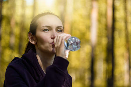 closeup brunette woman quenches thirst, drinks water from bottle in Park