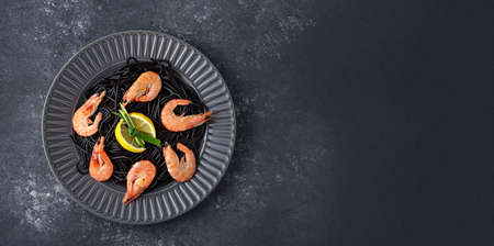 top view black pasta with ink cuttlefish, Royal shrimp and lemon slices in gray plate on gray background with copy space for banner, cooking at home, quarantineの写真素材