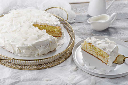 homemade coconut white cake on white background, portion of cake on plate with spatula, home cookingの写真素材