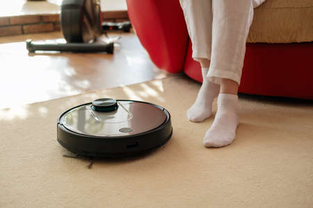 Robotic vacuum cleaner and legs on carpet, lazy and comfortable home, slow living concept, restの写真素材