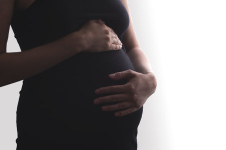 closeup silhouette of pregnant woman in black dress with hand on belly on white background, happy healthy pregnancyの写真素材
