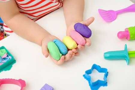 close up children's hands with colored plasticine, play dough, molds for modeling on white...