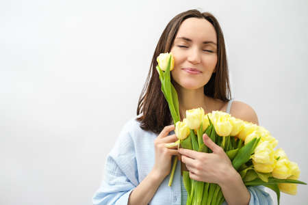portrait beautiful brunette woman with closed eyes enjoys bouquet of yellow tulipsの写真素材