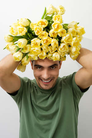 vertical portrait smiling man in green T-shirt with bouquet of flowers, yellow tulips on his head,...