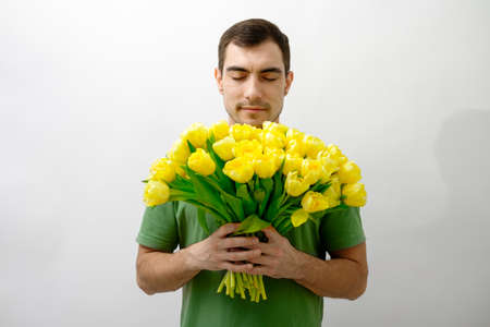 portrait man in green T-shirt with closed eyes enjoy bouquet of flowers yellow tulips in hand,...