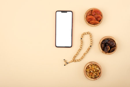 Top view of smartphone with white screen, rosary lying next to dried fruits, religious concept, love of Islam, copy space, mockupの写真素材
