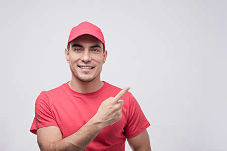 portrait of man in red T-shirt and cap shows finger up on white background, courier, delivery...