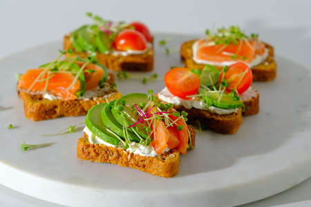 closeup healthy toast with salmon, trout, cherry tomatoes, avocado and microgreens on white marble board, healthy breakfastの写真素材