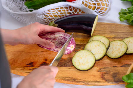 women's hands cut eggplant with knife on wooden Board, process of cooking moussaka, ratatouilleの写真素材