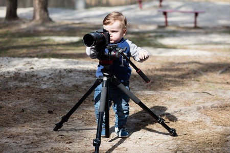 Young photographer child taking photos with a camera on a tripodの写真素材