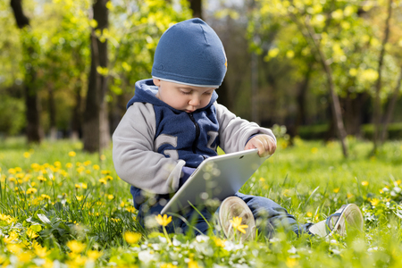 Child playing with tablet outdoors. Cheerful child with a portable PC in your hands.の写真素材