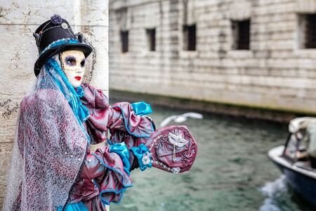 Blue masked carnaval costume with hat catching a ride next to famous Bridge of Sighs, Venice,Italy.の写真素材