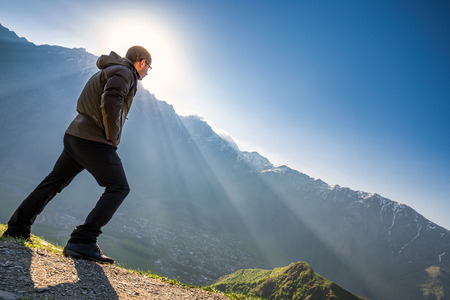 Man overlooking the mountains standing agains strong wind at Gergeti Trinity Church also known as Tsminda Sameba on the background of a mountain ridge and clouds, Stepantsminda, Kazbegi, Georgia.の写真素材