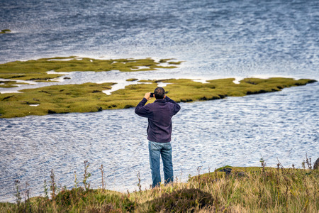 Man taking photo of Scottish mountains during sunset in Autumn on the Isle of Skye, Scotland, UK.の写真素材