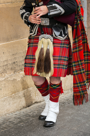 Scottish bagpiper dressed in traditional red and black tartan dress stand.の写真素材