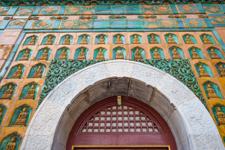 The wall above the doorway, decorated with many oriental statues of gold color, China.の写真素材