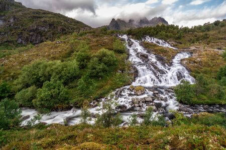Beautiful waterfall among the autumn forest and mountains. on the road to Mount Munken and to the houses of Munkebu on the Lofoten Islands, Norwayの写真素材