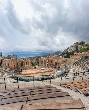 Catania, Italy - October 02 2017: Ruins of the Ancient Greek Theater in Taormina, Sicily with the smoke tail over Etna extending over the the Giardini-Naxos bay of the Ionian Sea in the rainy day.のeditorial素材