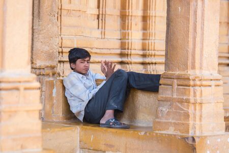 Jaisalmer, India - March 10 2017: A sad boy is sitting on a stone bench outside.のeditorial素材