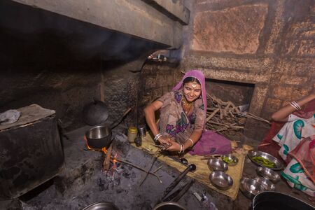 Jodhpur, India - March 08 2017: A woman with a smile puts more firewood on the fire for cooking in the kitchen in the village.のeditorial素材