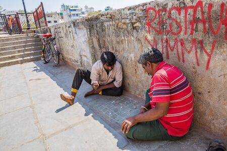 Udaipur, India - March 04 2017: Two men play a game on the ground. They sit with a shadow and are...