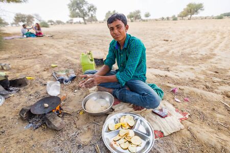 Jaisalmer, India - March 09 2017: A man prepares food on the fire in the desert. He fries balls of...
