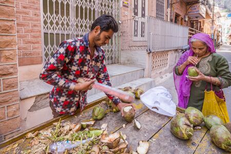 Jodhpur, India - March 07 2017: A man sells coconuts on the street. Nearby stands a woman and drinks fresh coconut milk.のeditorial素材