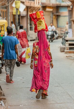 Jodhpur, India - March 07 2017: Blue walls of the city and woman hold bag of rice on the head.のeditorial素材