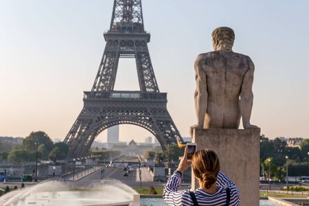 Beautiful girl takes a photo with smartphone of the famous Eiffel Tower in Paris, France.の写真素材