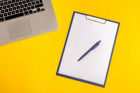 Flat lay out. Computer on yellow background with paper folio and pen. Business concept idea. Copy...