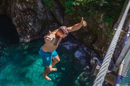 Man jumping from the swing bridge on Blue Pool in Wanaka, New Zealand.