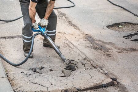 Closeup of a photo of professional workers in uniform repairing asphalt road with a jackhammer. Concept renovation, major repairs of the main street in city, road construction.の写真素材