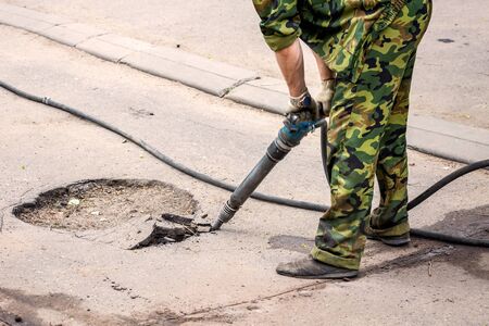 Closeup of a photo of professional workers in uniform repairing asphalt road with a jackhammer. Concept renovation, major repairs of the main street in city, road construction.の写真素材