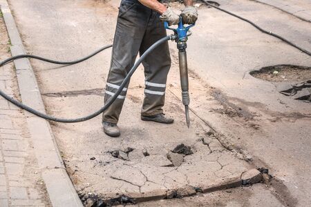 Closeup of a photo of professional workers in uniform repairing asphalt road with a jackhammer. Concept renovation, major repairs of the main street in city, road construction.の写真素材