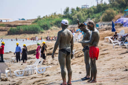 Tourists applying Dead Sea mud which possesses the medicinal qualities and helps to the people with skin problems. Body care treatment in Israel. Dead Sea, Israel - April 19 2018のeditorial素材