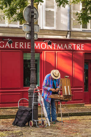 Painter with red wall behind him on Montmartre hill. Montmartre with traditional french cafes and art galleries is one of the most visited landmarks in Paris. Vertical image. Paris, France - July 28 2018.のeditorial素材
