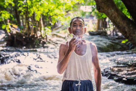 Local old man smoking a cigarette in white t-shirt at Rainforest of Doi Inthanon. Chiang Mai, Thailand - November 10 2017.のeditorial素材
