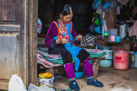 Long neck old tribal woman sits on a bed wearing traditional clothes. Chiang Mai, Thailand - November 12 2017.のeditorial素材