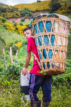 Tribal boy stands by the road in the jungle with a big basket. Chiang Mai, Thailand - November 11 2017.のeditorial素材