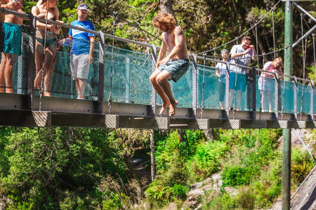 People jump from the swing bridge on Blue Pool in Wanaka, New Zealand. Mount Aspiring, New Zealand - December 22 2017.のeditorial素材