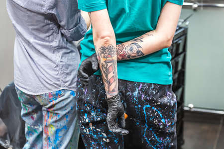 A couple of hairdressers with colored hair and bright tattoos paint the head of an attractive girl in purple. Minsk, Belarus - April 14 2020.のeditorial素材