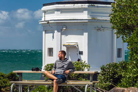Man sits on a bench near lighthouse at Bluff, New Zealand. Bluff, New Zealand - December 19 2017.