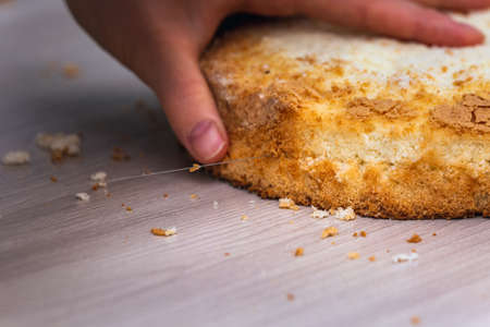 Female hand cuts sponge cheesecake with coconut, on wooden table.