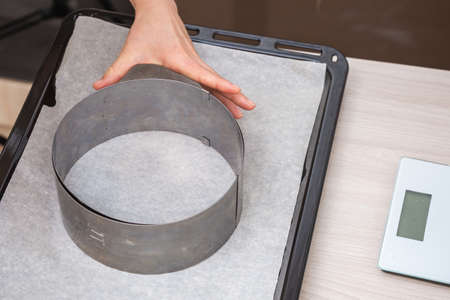 Hand holds iron cake form on baking paper on a tray. Preparing homemade cake.