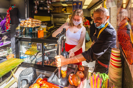 Local Turkish man makes a fresh pomegranate juice at his fruit stall for happy young tourist. Pomegranate juice is a famous local beverage in Turkey. Istanbul, Turkey - September 30 2020.のeditorial素材